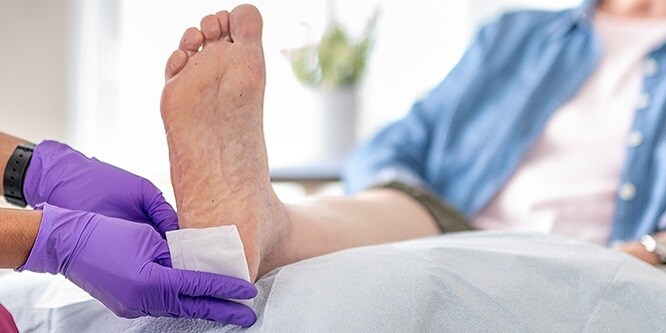 Eine Krankenschwester klebt ein Pflaster auf die Ferse eines Patienten
