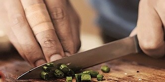 Ein Mann schneidet auf einem Küchenbrett Schnittlauch
